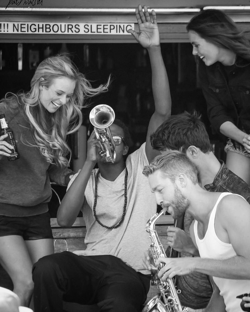 Caption: A black and white photo of a group of young musicians playing music and enjoy themselves under a sign that reads, “Neighbours sleeping.” (Local Guide @Mongoose)