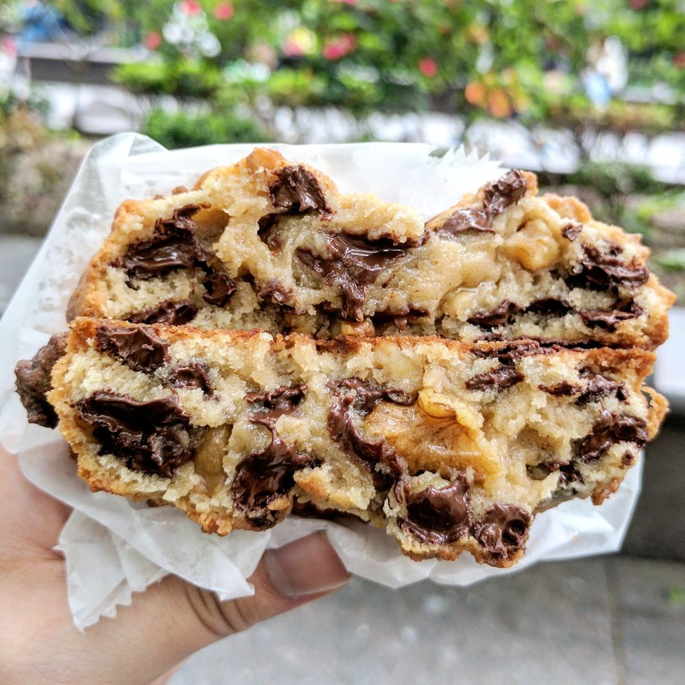 Caption: A photo of a hand holding two halves of a chocolate chip walnut cookie from Levain Bakery in New York City. (Local Guide Bernard Lin)