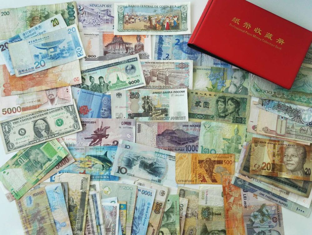 描述：一张不同货币的钞票的照片散布在白色的桌面上。在右上角可以看到一本红色的纸币收藏册。(本地向导 @TsekoV)