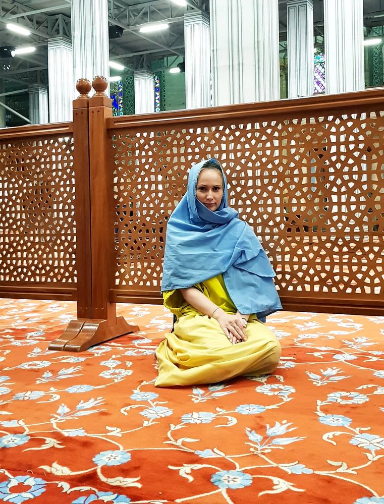 Caption: A photo of Google Moderator @Petra_M dressed in a yellow dress and wearing a blue scarf over her head, sitting inside the Blue Mosque in Istanbul, Turkey. (Local Guide @Petra_M)