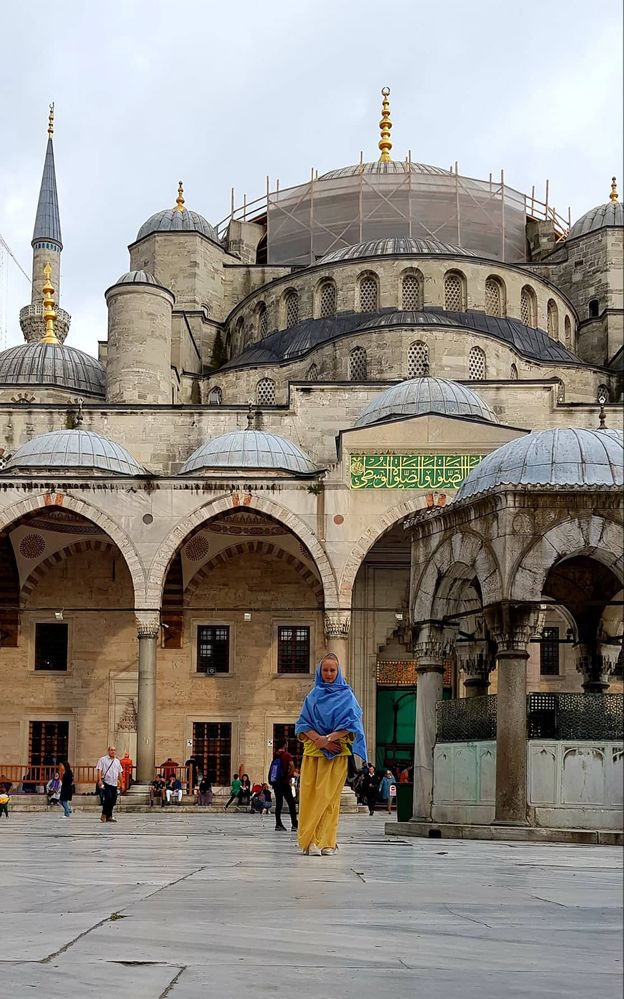 Caption: A photo of Google Moderator @Petra_M dressed in a yellow dress and wearing a blue scarf over her head, standing in front of the Blue Mosque in Istanbul, Turkey. (Local Guide @Petra_M)