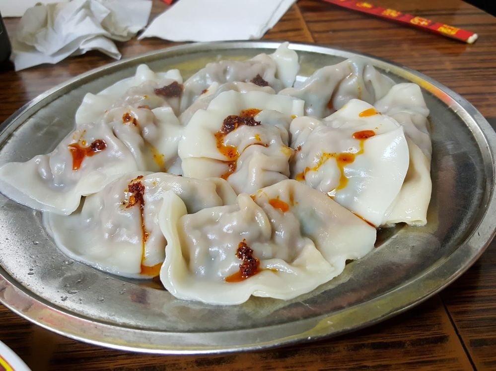 Caption: A photo of steamed dumplings with chili oil drizzled on them on a metal plate at 88 Lan Zhou Handmade Noodles in New York City. (Local Guide Walter Lee)