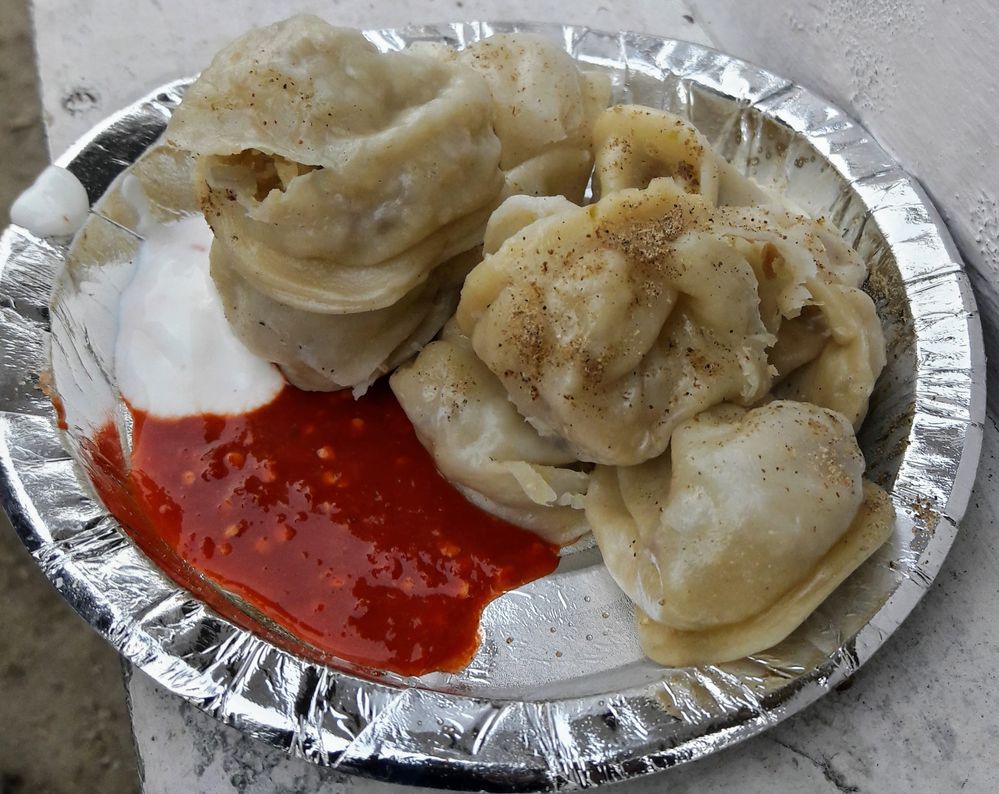 Caption: Momos kept in a silver plate with sauce placed on a white wooden table.