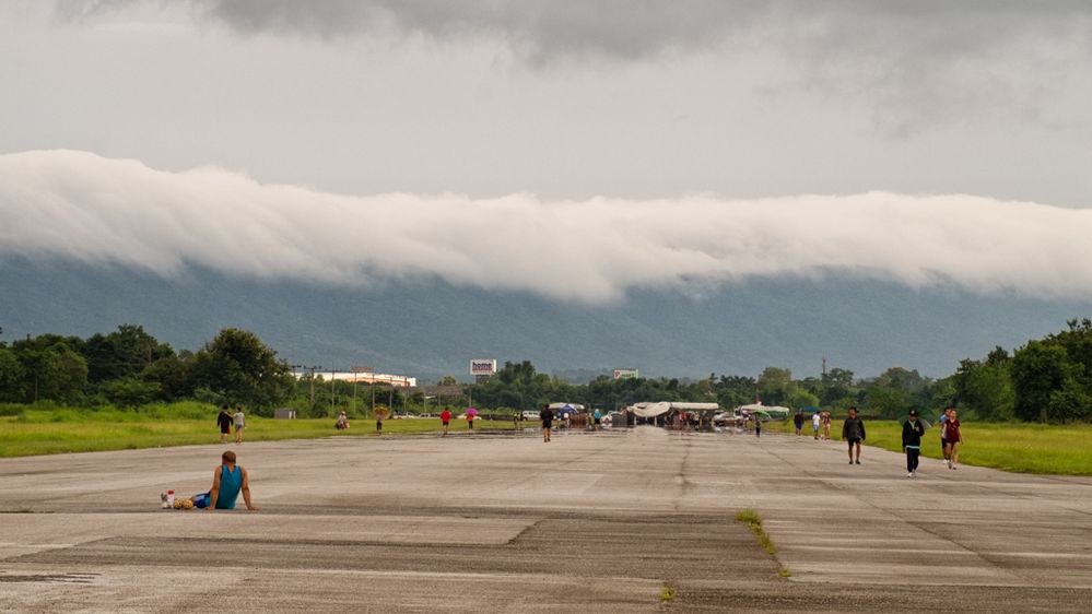 A cloud hugs the top of this mountain range . Chiang Rai Old Airport is in the foreground.