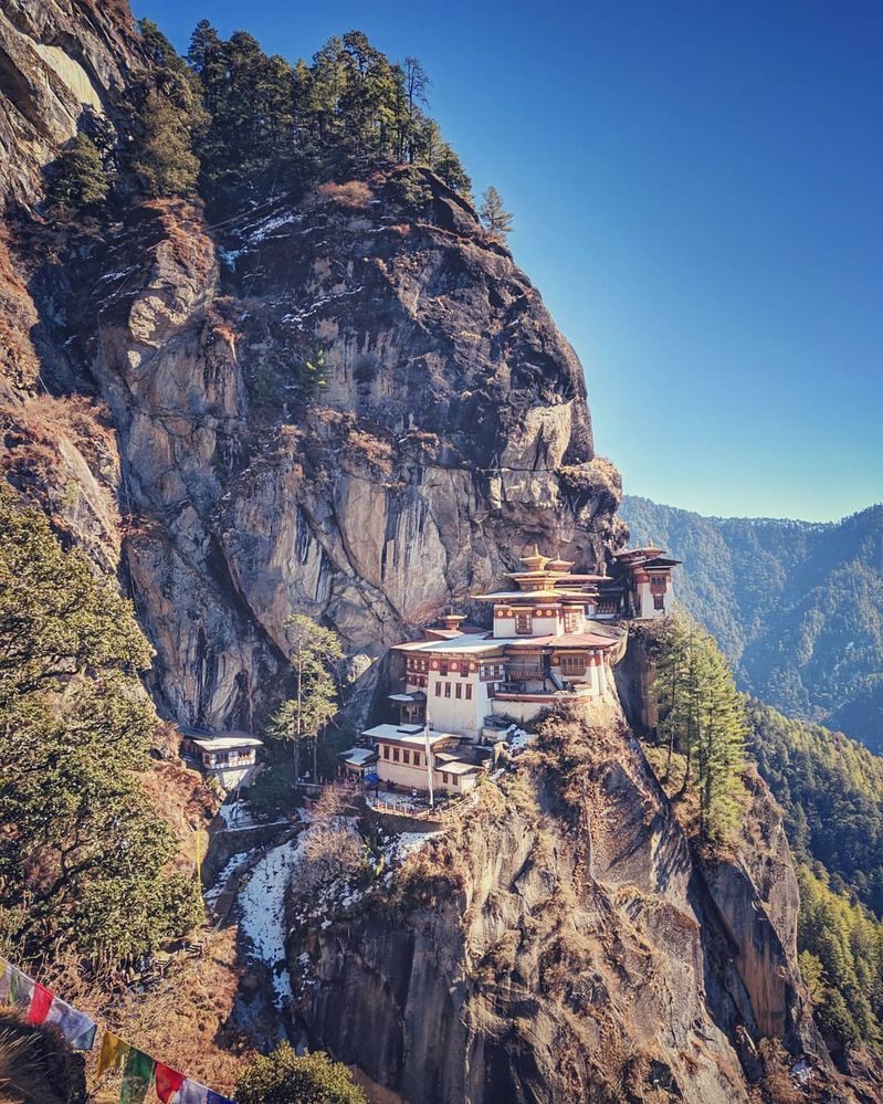 Caption: A photo of the white buildings of the Tiger’s Nest monastery in Bhutan, perched on a mountainside. (Local Guide @Venky61)