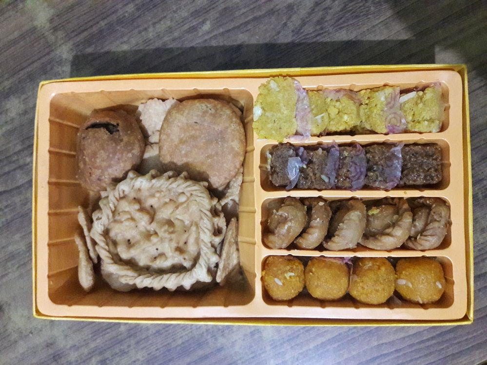 A box containing various kinds of sweets (barfi, laddu) and some snacks.