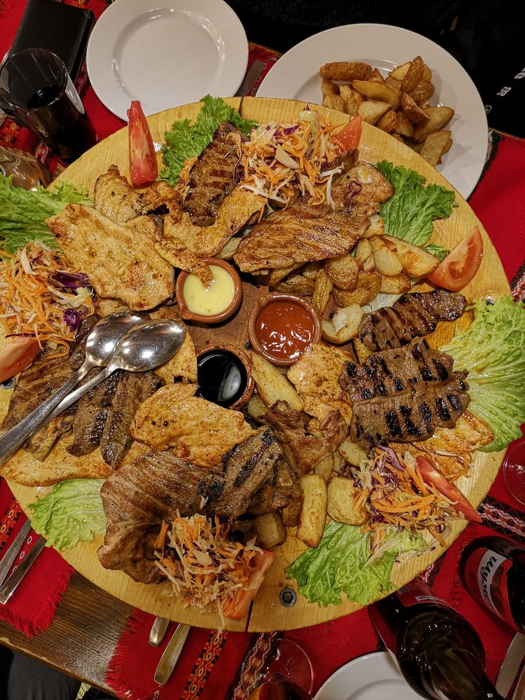 Billedtekst: Et billede af oksebøffer og kyllingefilleter, ristede kartofler, salat, tre slags dyppelse og to skeer på en træplade på en en traditionel Bulgarsk restaurant (Local Guide @MortenSI)