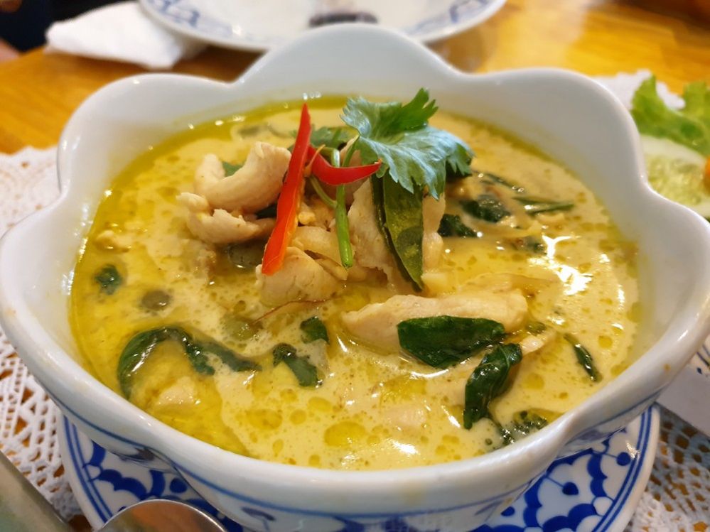 Caption: A close-up photo of green chicken curry with bit of chicken meat, spicy chili, and herbs in a white bowl. (Local Guide suchai Kruewaisayawan)