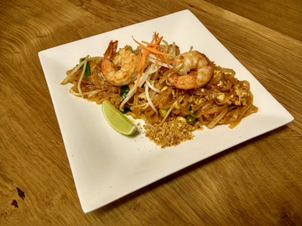 Caption: A photo of pad thai noodles with shrimps, vegetables, peanuts, and a slice of lime for decoration, served on a white plate. (Local Guide Nut Teppimol)