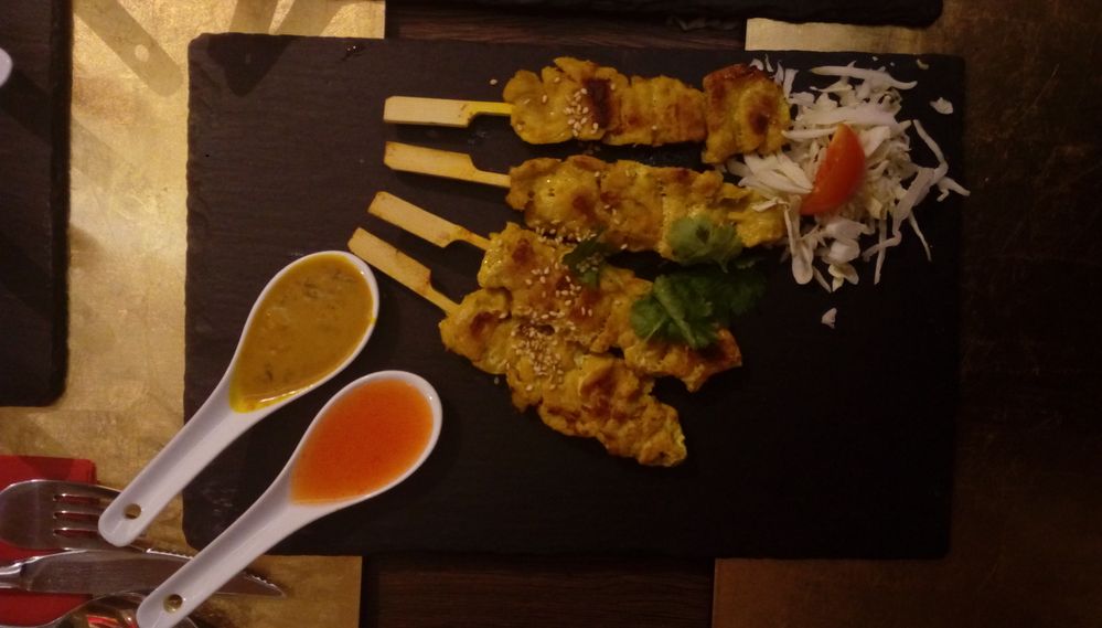 Caption: Four sticks of Chicken satay with a spoon full of  sweet and sour sauce, as well as a spoon full with a peanut sauce. (photo by KlaudiyaG)