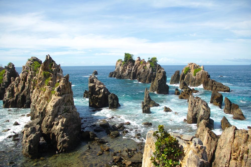 Caption: A photo of rock formations in the water taken at Shark Teeth Coast in Lampung, Indonesia on a partly cloudy day. (Local Guide @ibadahmimpi)
