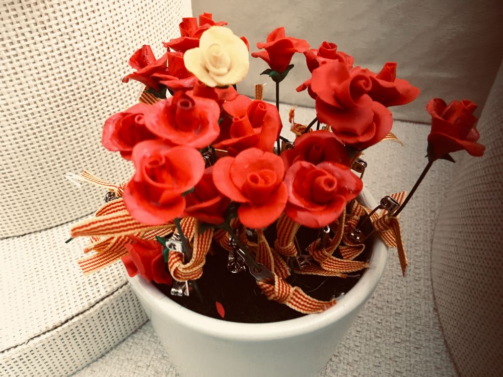 Caption: A flower pot filled with tiny red rose brooches made of clay and decorated with the Catalan flag.