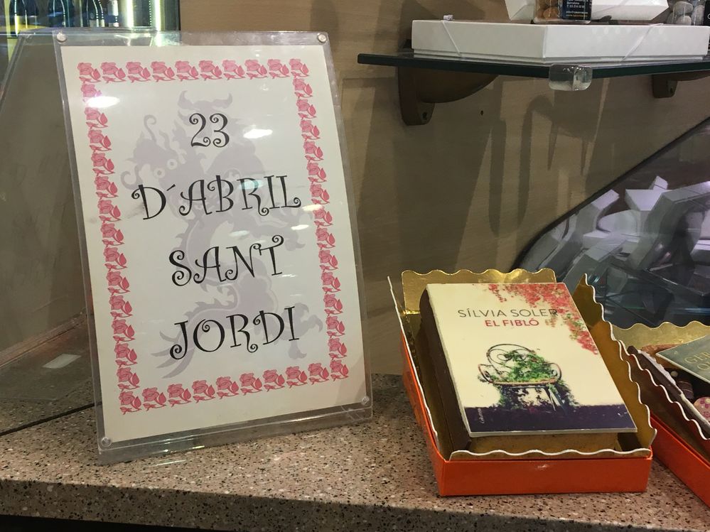 Caption: A notice displaying a date  next to a book made of chocolate in a bakery window.