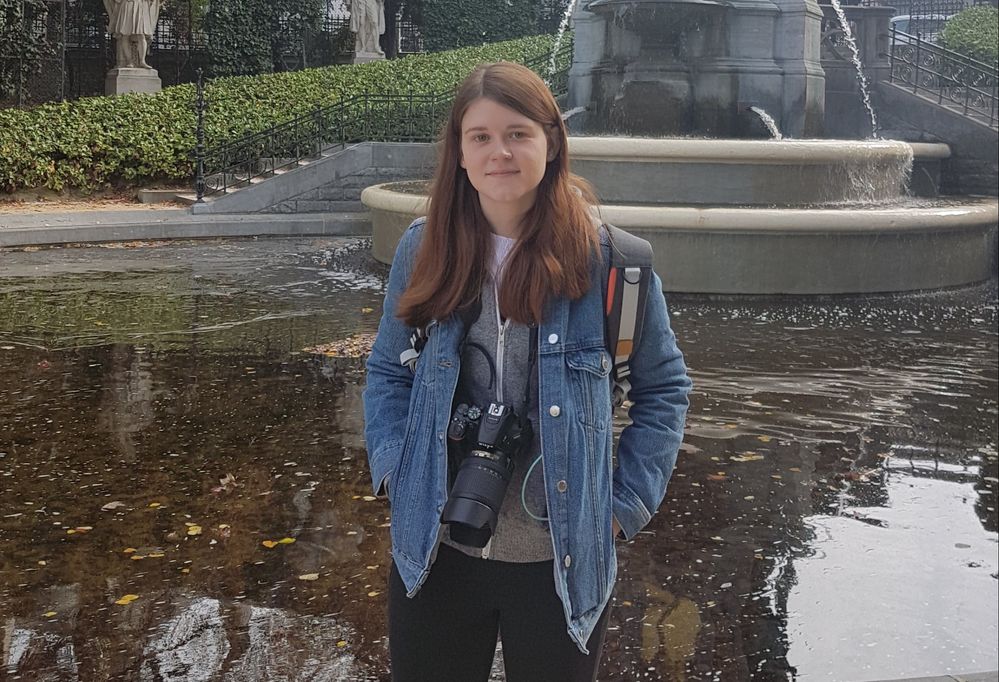Caption: A photo of Local Guide Jesi posing in front of a fountain while wearing her DSLR camera around her neck. (Courtesy of Local Guide @Jesi)