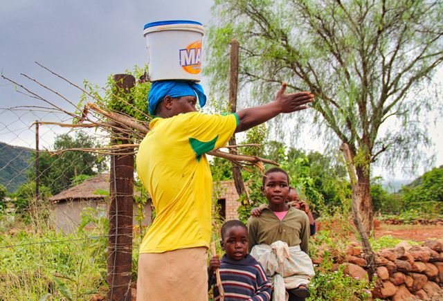 In the early morning a woman fetching firewood and carrying a bucket of fresh water on her head, with her three children beside her, indicates the direction in which to go to reach the Ga-Mokgotho Community Hall. Photo Credit: Local Guide Leora Hart.