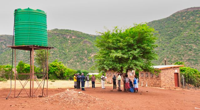 Locals from the Ga-Mokgotho village gather outside the town hall, awaiting the day's events. A large green jojo tank can be seen alongside them. Photo credit: Local Guide Leora Hart