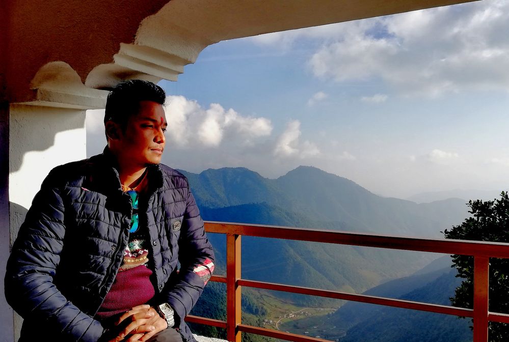 A photo of local guide@Mr_Prach sitting at the lobby and the views from Chandragiri Hills behind.