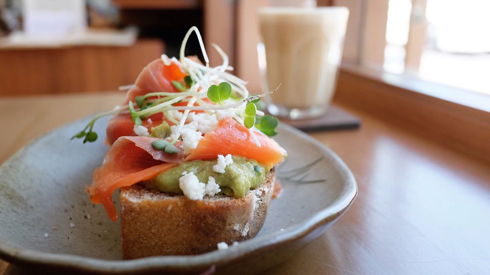 Caption: A photo of avocado toast topped with smoked salmon, cheese, and microgreens next to a window at Flour Flour slice in Chiang Mai, Thailand. (Local Guide Aikapat Sittichai)