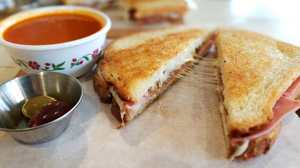 Caption: A photo of a pulled-apart grilled cheese sandwich next to a cup of tomato soup and small metal bowl with olives. (Local Guide Sang-Duk Seo)