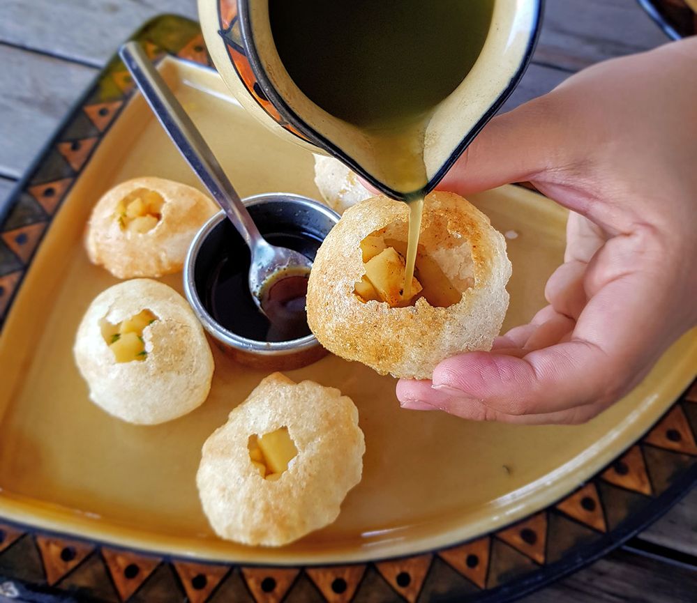 Caption: A closeup photo of hands pouring mint water into panipuri at Bhoj Restaurant in Victoria, Australia. (Local Guide Melb_belly Rza Lam)