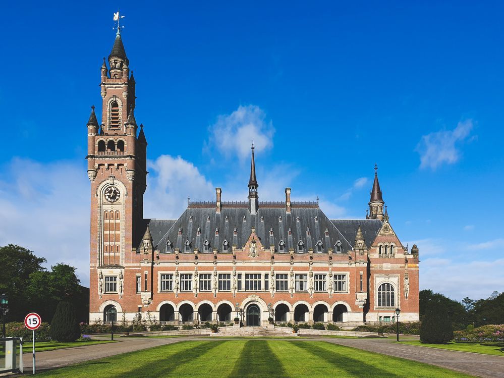 Caption: A photo of the red facade of the Peace Palace in The Hague, The Netherlands, against a bright blue sky. The lawn in front of the palace is freshly mowed and green. (Local Guide @SunPanupong)