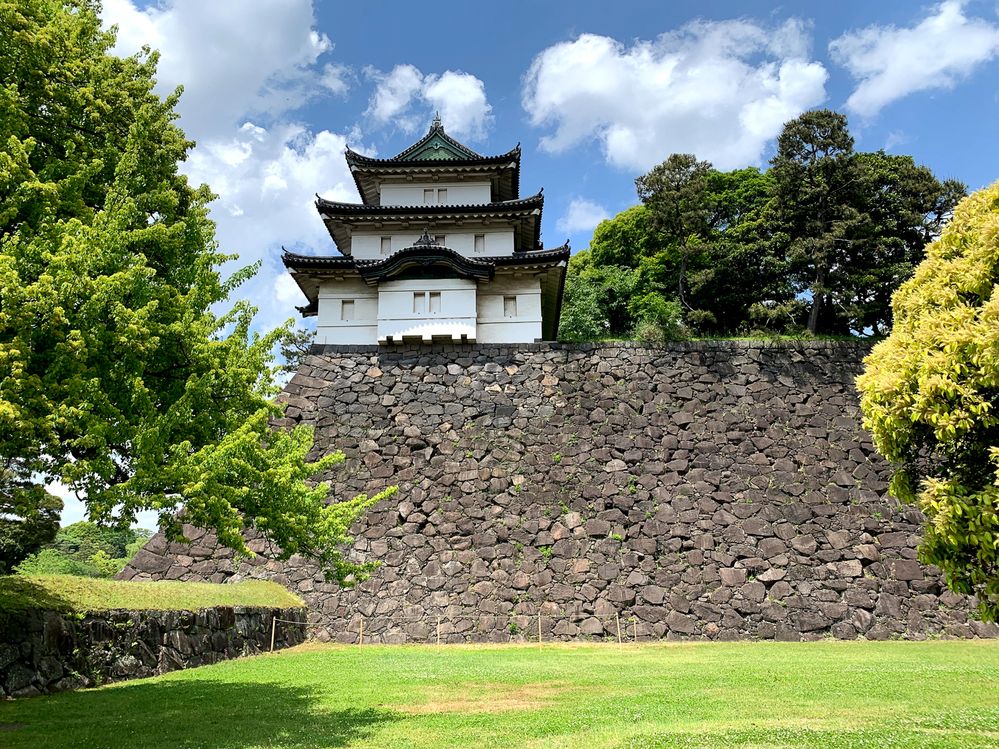 Caption: A photo of the exterior of the Imperial Palace in Tokyo, Japan, with grass and trees surrounding it, taken on a partly cloudy day. (Local Guide  飯野博之)