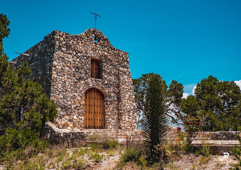 Caption: A photo of the exterior of a stone church with a wooden door. A cross is located at the top of the church. (Ricardo M. Braham)