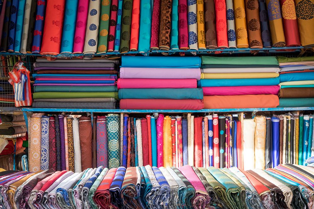 Caption: A close-up photo of bolts of multi-colored fabric on display in a market. (Local Guide Michael Turtle)