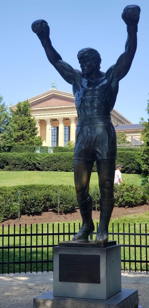 Caption: a photo of the Rocky's statue with his arms up straight in a "victory" pose with Philadelphia Museum of Art on the background. (Local Guide @FelipePk)