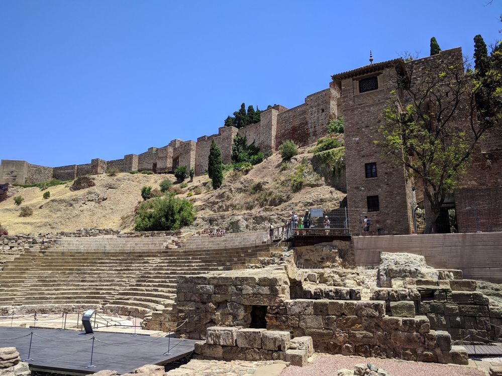 Caption: A photo of the ruins of the Roman Theatre in Malaga with a part of the Alcazaba fortress walls in the background. (Local Guide @MoniDi)
