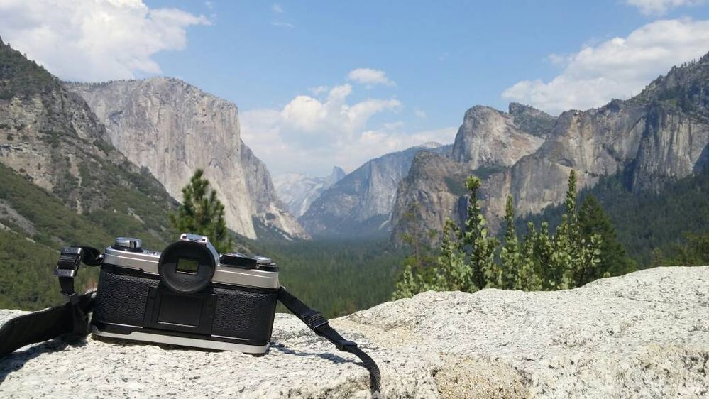 Caption: A photo of a camera sitting on top of a rock ledge, overlooking the mountain range and valley of Yosemite National Park in California, USA. (Local Guide Joey)