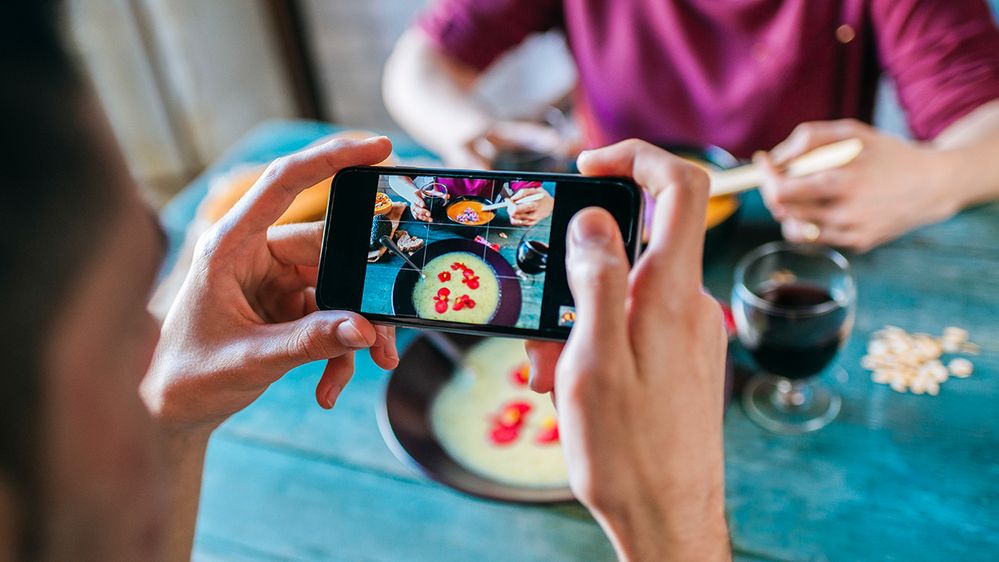 Caption: A photo that shows a person’s hands as they capture a photo of the dish in front of them using their smartphone. (Getty Images)