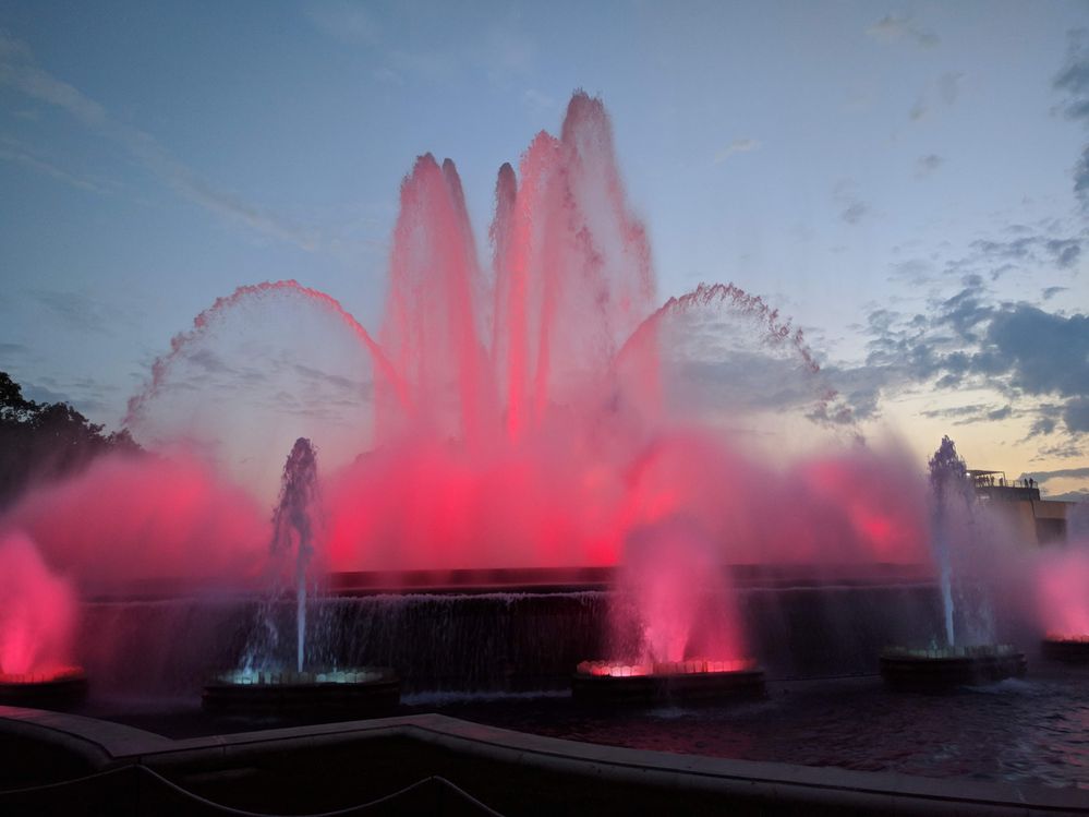 Caption: A photo of the Magic Fountain of Montjuic lit up in bright pink at dusk. (Local Guide @MoniDi)
