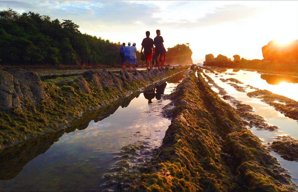 Caption: A photo of a sunrise over a water channel in Serang, Indonesia, with a group of people walking along the edge of the channel. (Local Guide @pyerdna)