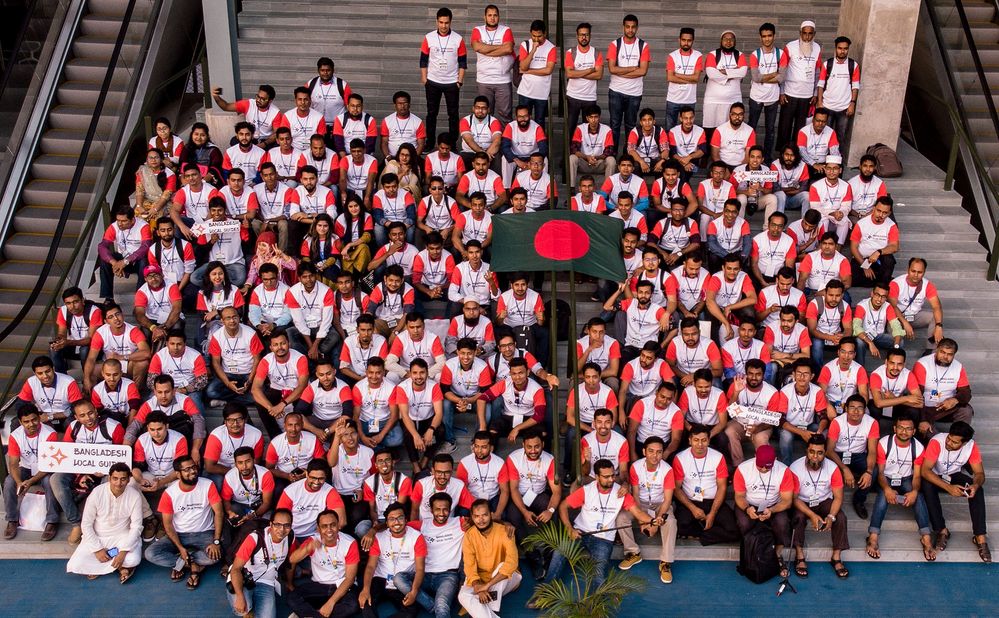Caption: A Group Of Local Guides sitting in stairs and some of are stand in back side and a Bangladeshi Flag on Middle of  the group photo
