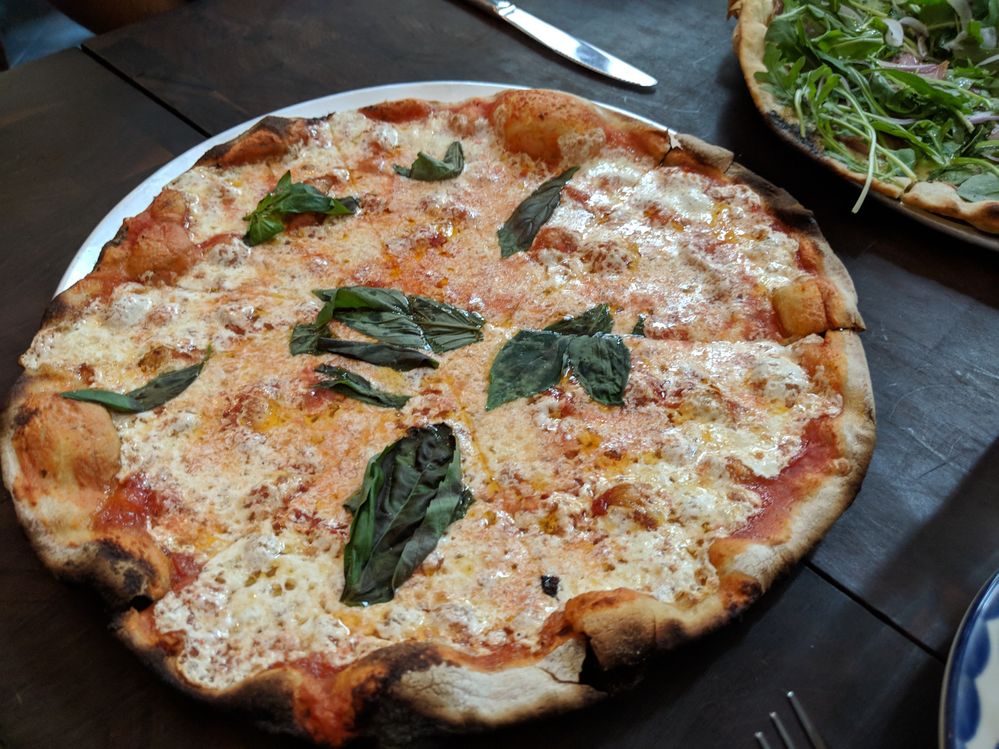 Caption: A photo of a large margherita pizza on a wooden table at Marta in New York, NY. (Local Guide Andres A.)