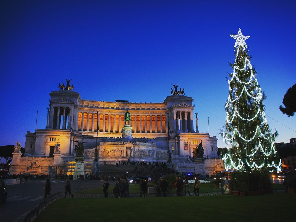 Caption: A photo of a Christmas tree decorated with lights and a bright star tree-topper in front of Altar of the Fatherland in Rome, Italy. (Local Guide Lionel Hocepied)