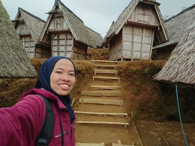 Caption: A photo of Local Guide @Nyainurjanah taking a selfie in front of traditional Indonesian buildings for storing rice. (Local Guide @Nyainurjanah)