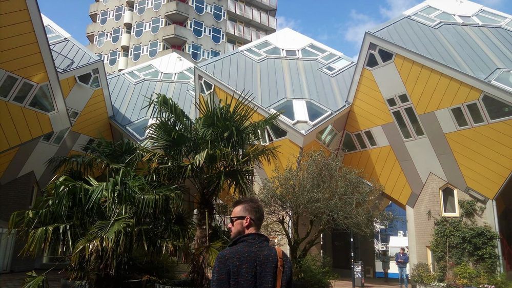 Caption: A photo of Google Moderator @BorrisS in front of the grey and yellow Cube Houses in Rotterdam, The Netherlands.