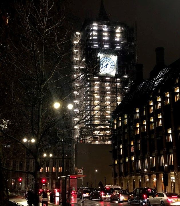 Legenda: Uma foto do Big Ben tirada a noite, mostrando alguns casos e a Torre da Rainha com o relógio bem iluminado. (Local Guide @ItzPirk)