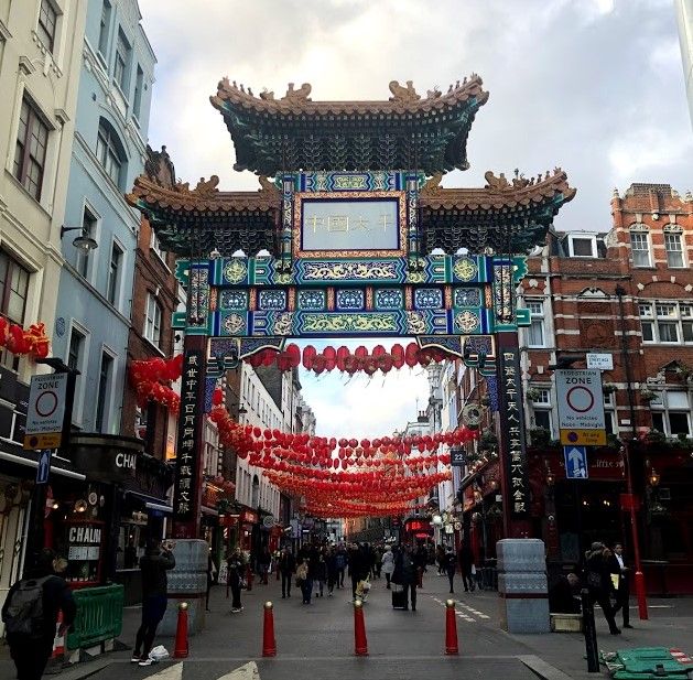 Legenda: uma foto do colorido Portão de Chinatown decorado com luminárias vermelhas e douradas e com várias pessoas indo e vindo. (Local Guide @ItzPirk)