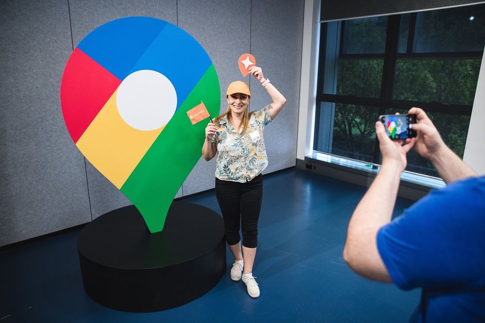 Local Guide Penny Christie standing in front of the new Google Maps logo, holding a Local Guides flag and logo and wearing an orange Local Guides hat, at Google Headquarters in Sydney during Google Maps 15th Birthday Media conference.