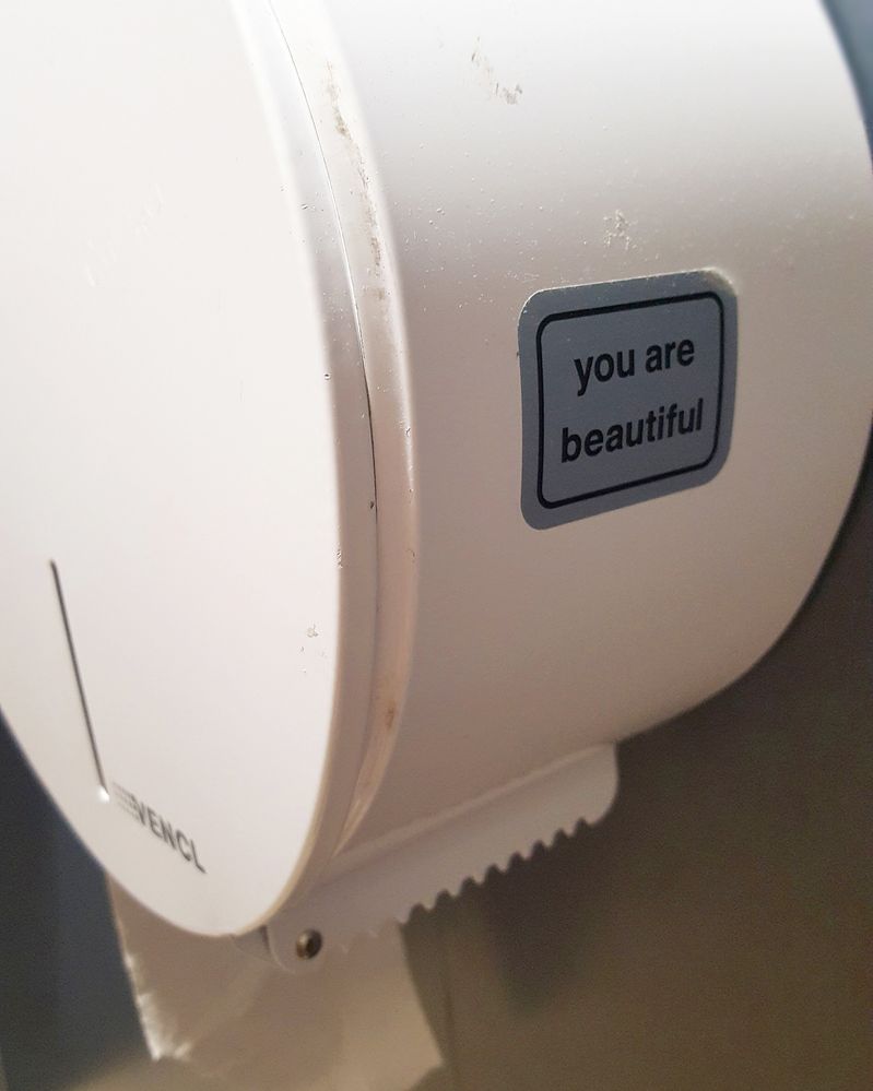 Caption: Toilet paper holder with a sticker that says: "you are beautiful".