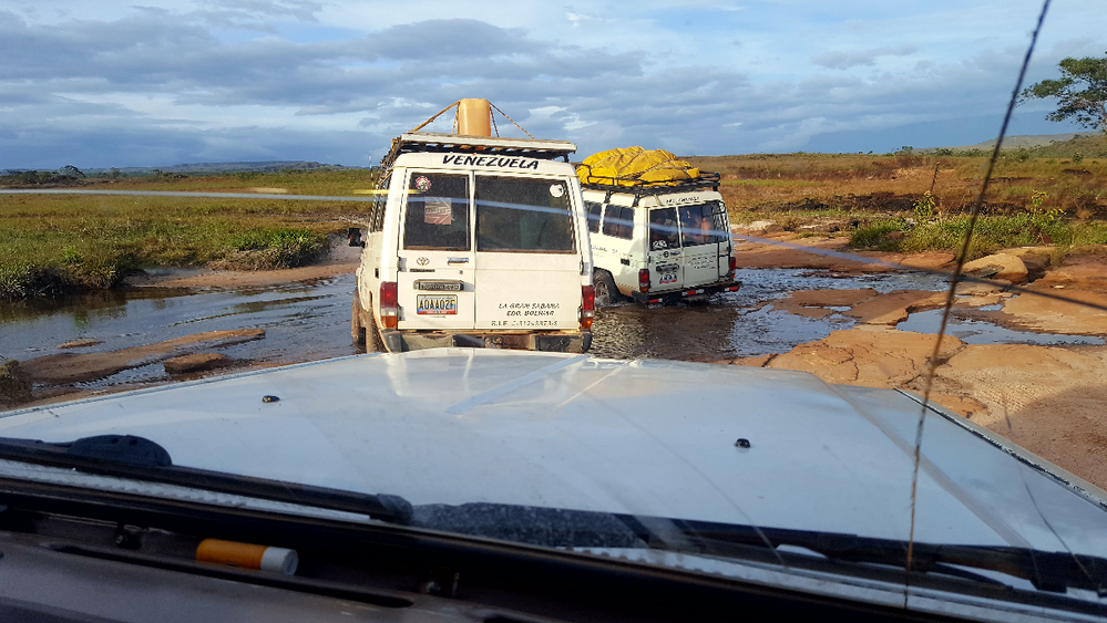 Caption: 4x4 cars on tour in the Gran Sabana, passing through a stretch of rocks and streams.