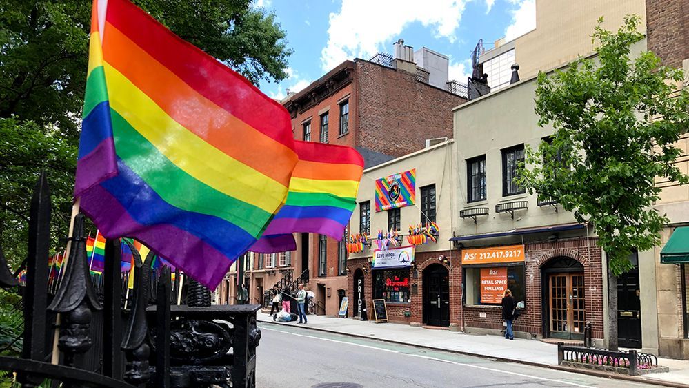 Caption: A photo of the exterior of Stonewall Inn in New York City, the “birthplace of Pride,” with rainbow flags flying outside. (Local Guide Darius Greulich)