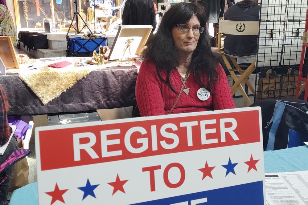 Caption: A photo of Stephanie Fritsch sitting at a table with a “register to vote” sign in front of her. (Local Guide Stephanie Fritsch)