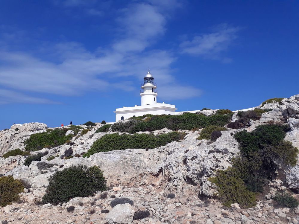 Caption: A photo of the white Cavalleria Lighthouse on top of a rocky cliff. (Local Guide @MoniDi)