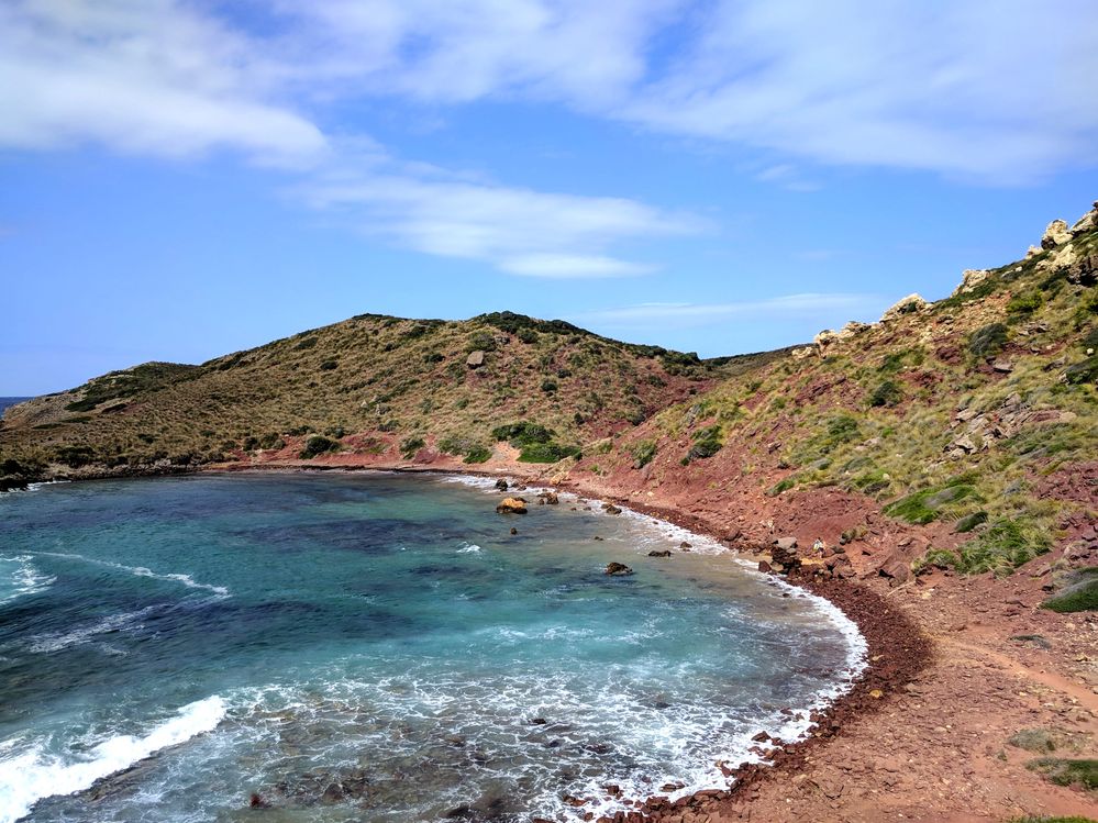 Caption: A photo of one of the crescent-shaped, red-soil Cavalleria Beaches. (Local Guide @MoniDi)
