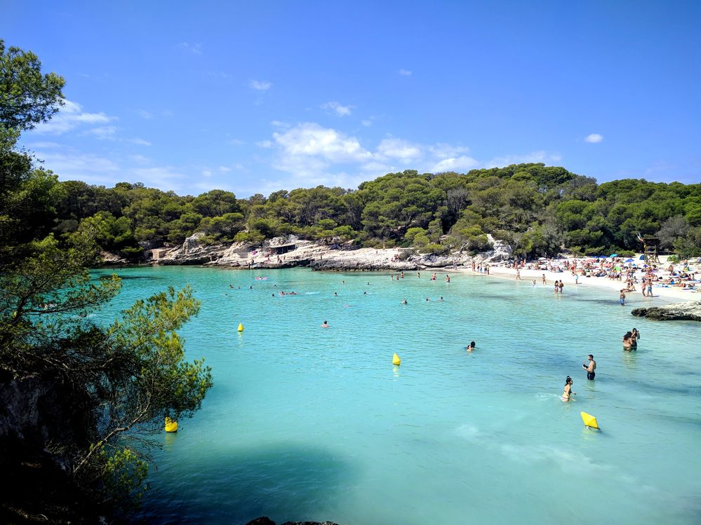 Caption: A photo of the turquoise water and the lush green trees at Cala en Turqueta Beach. (Local Guide @MoniDi)