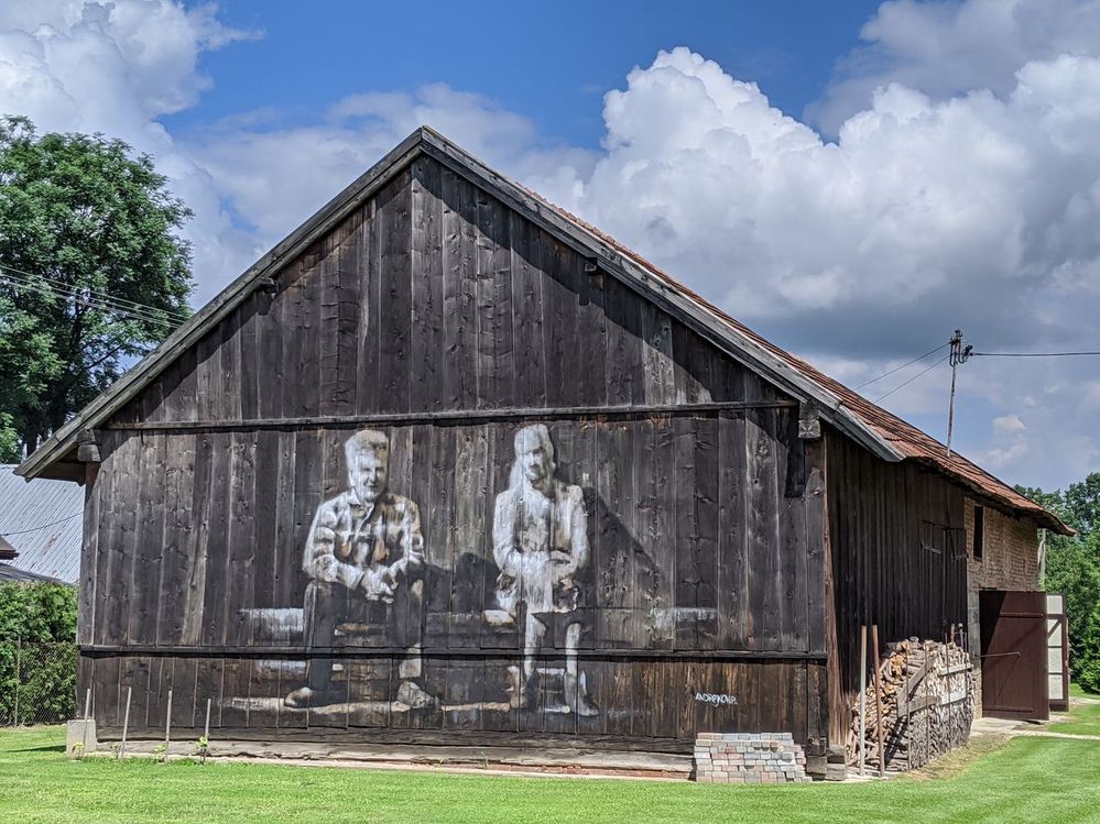 Painting on a wooden barn with a man on the left and a woman on the right, sitting on the bench.